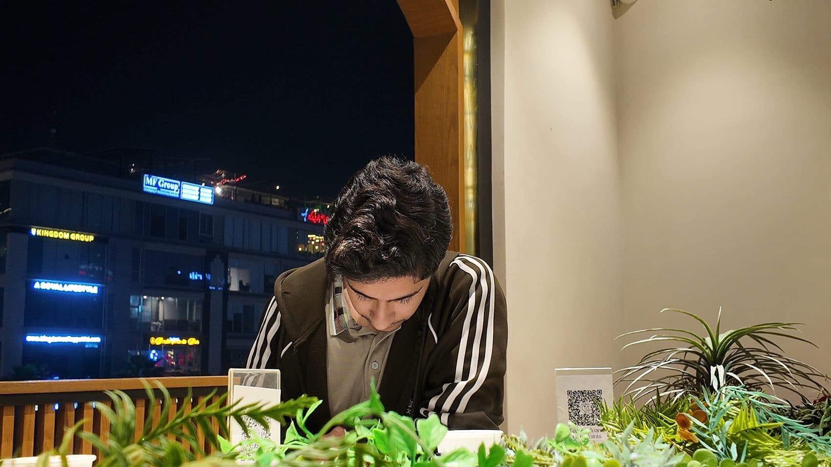 Night rooftop cafe, phone in hand with city lights behind