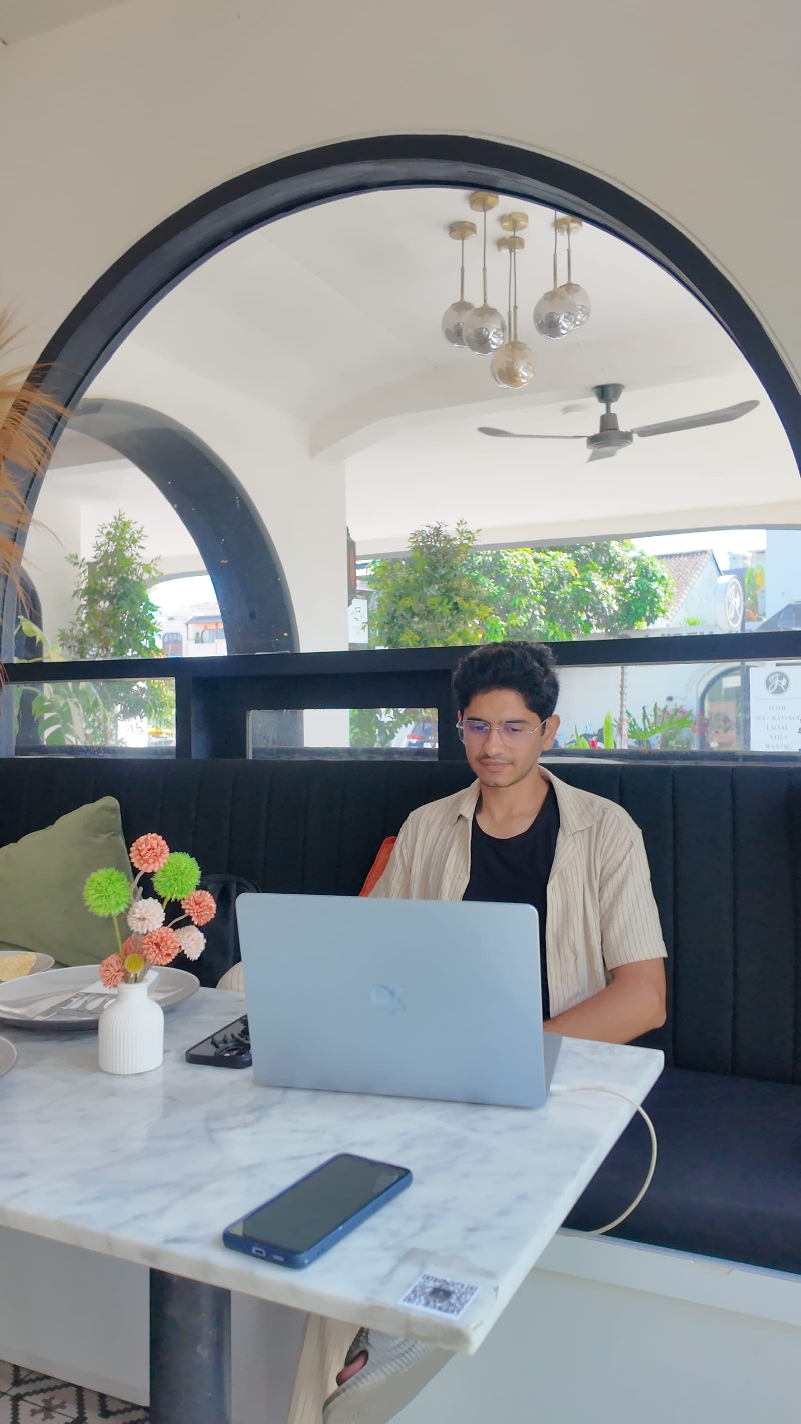 Waseem working under the cafe arch in Bali, blue polo, laptop open